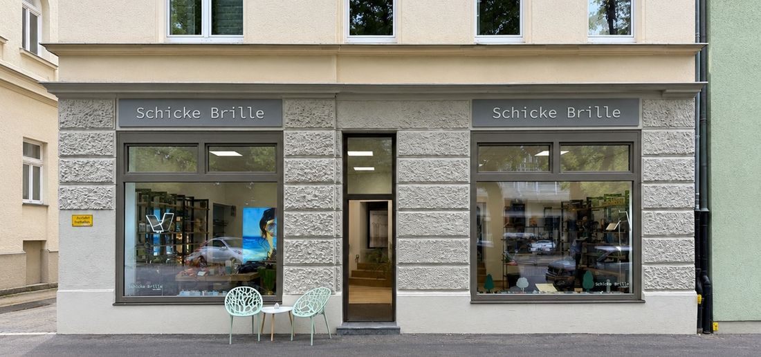Die Ladenfront in der Bismarckstraße 3: zwei Schaufenster mit Brillen, dazwischen die offene Eingangstür, davor zwei mintgrüne Stühle
